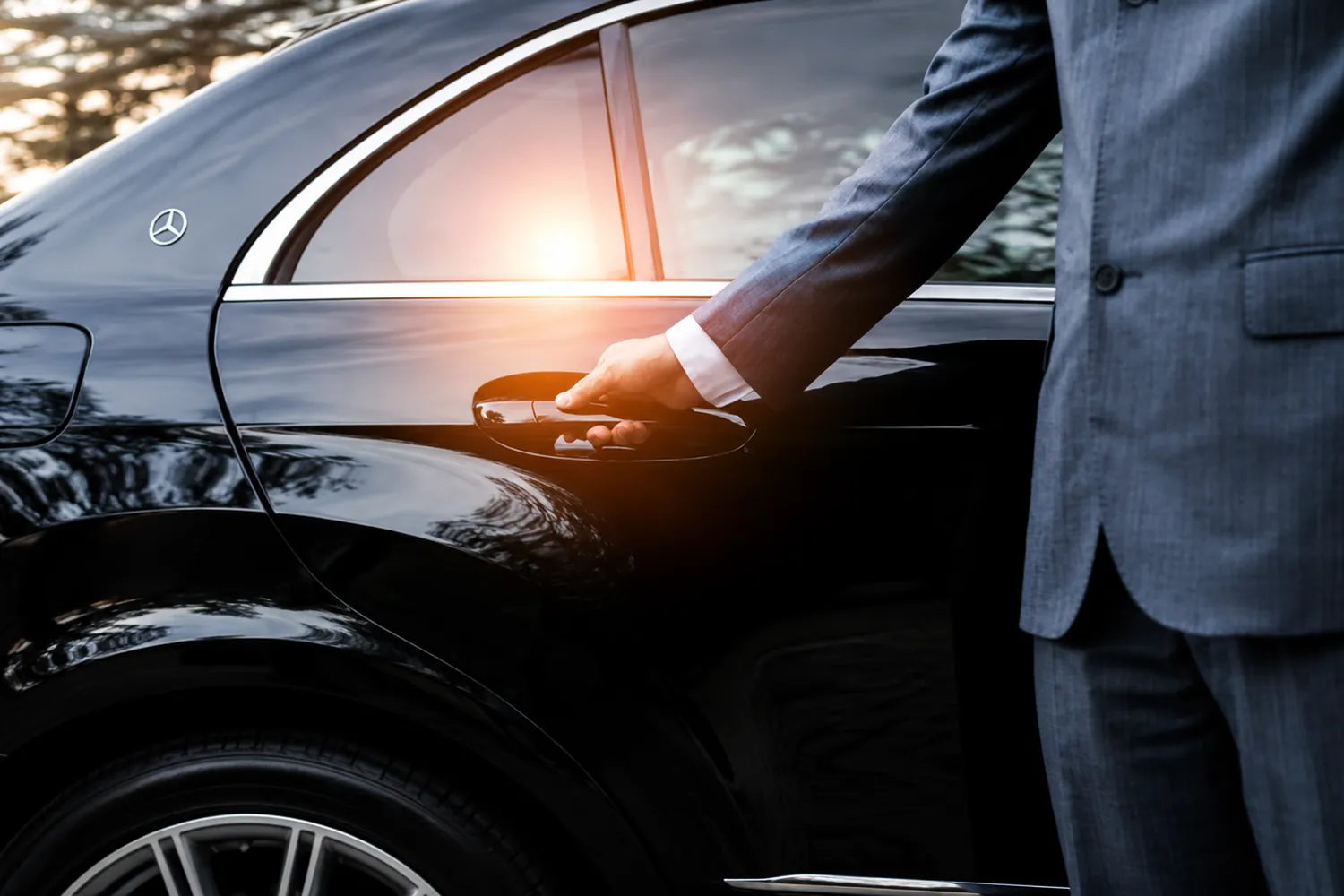Servizio Limousine Lugano - autista apre la portiera di una Mercedes Classe S Long nera al tramonto